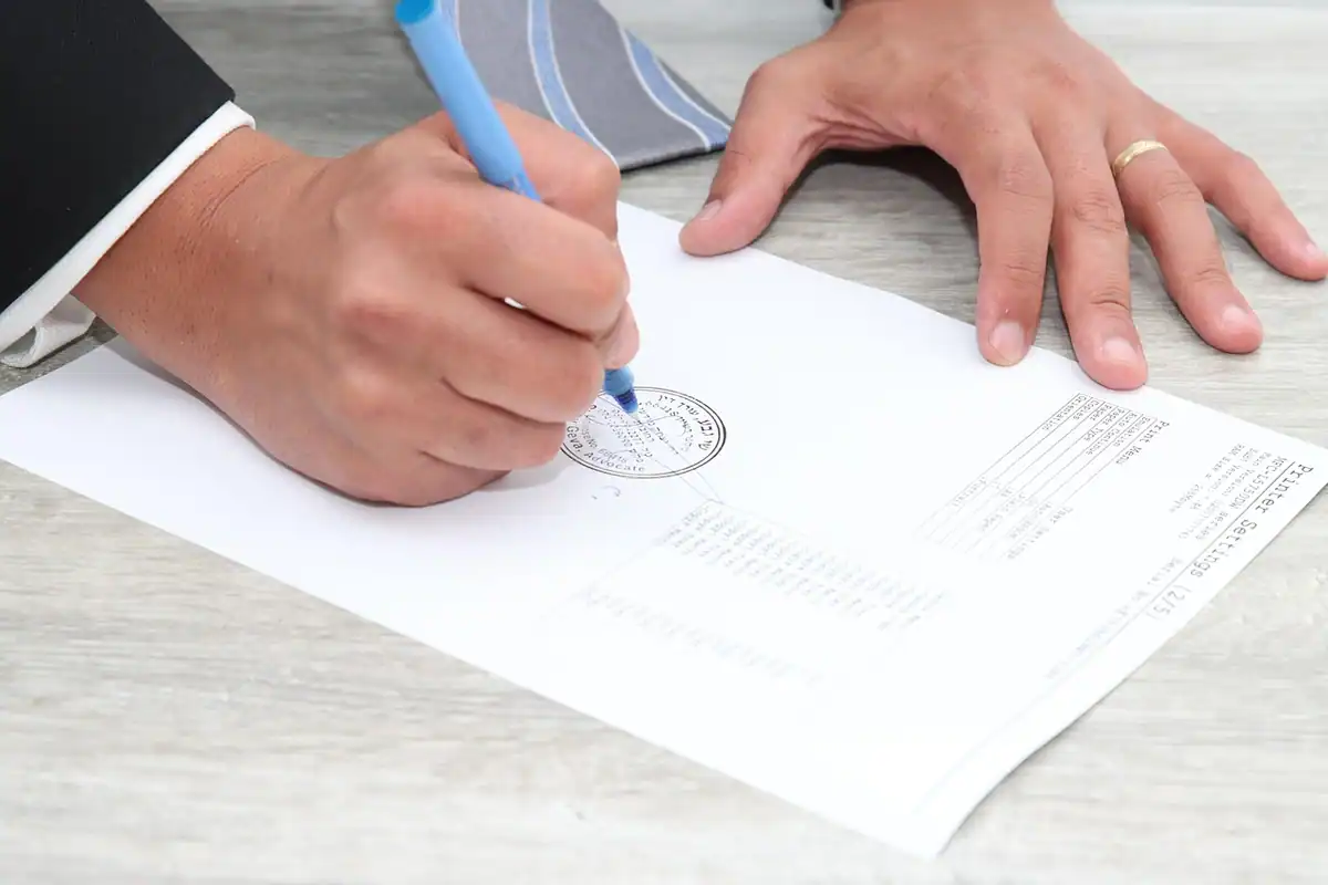 Mână care semnează un document oficial cu un sigiliu desenat pe foaie