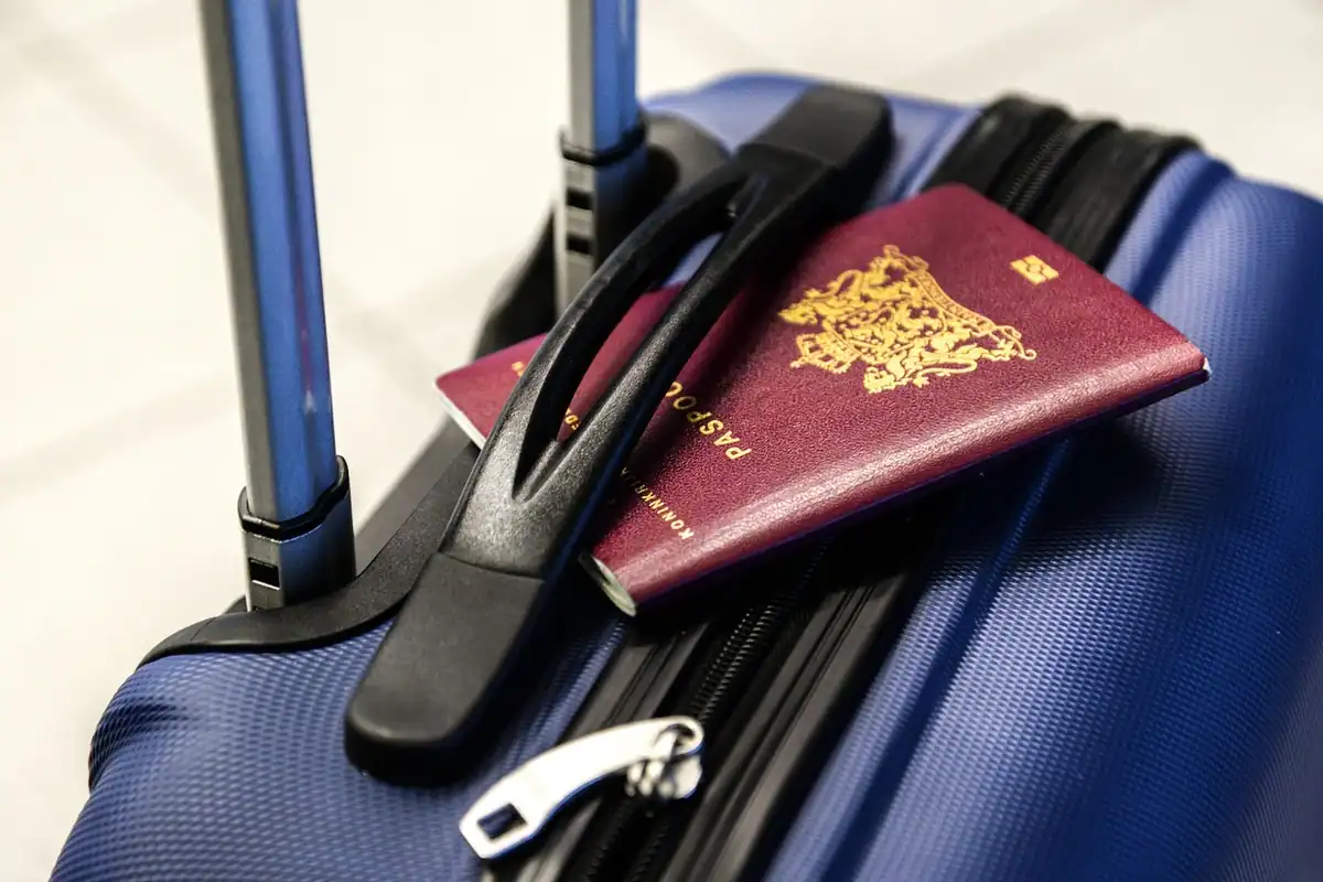 Pașaport bordo așezat pe un troley albastru, pregătit pentru o călătorie