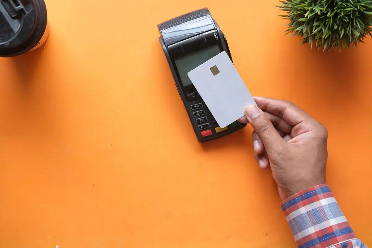 Card cu cip ținut în mână lângă un terminal de citire, pe fundal portocaliu