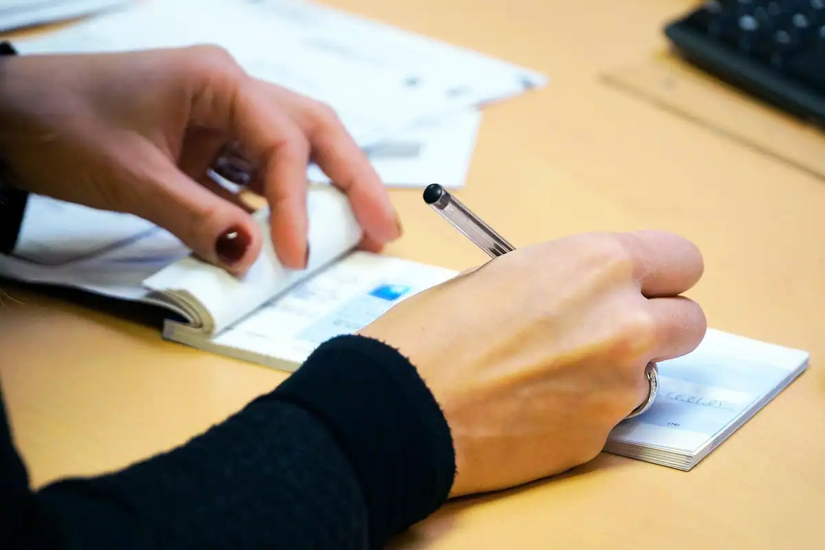 Mâini care completează cu pixul formulare pe un birou, în prim-plan