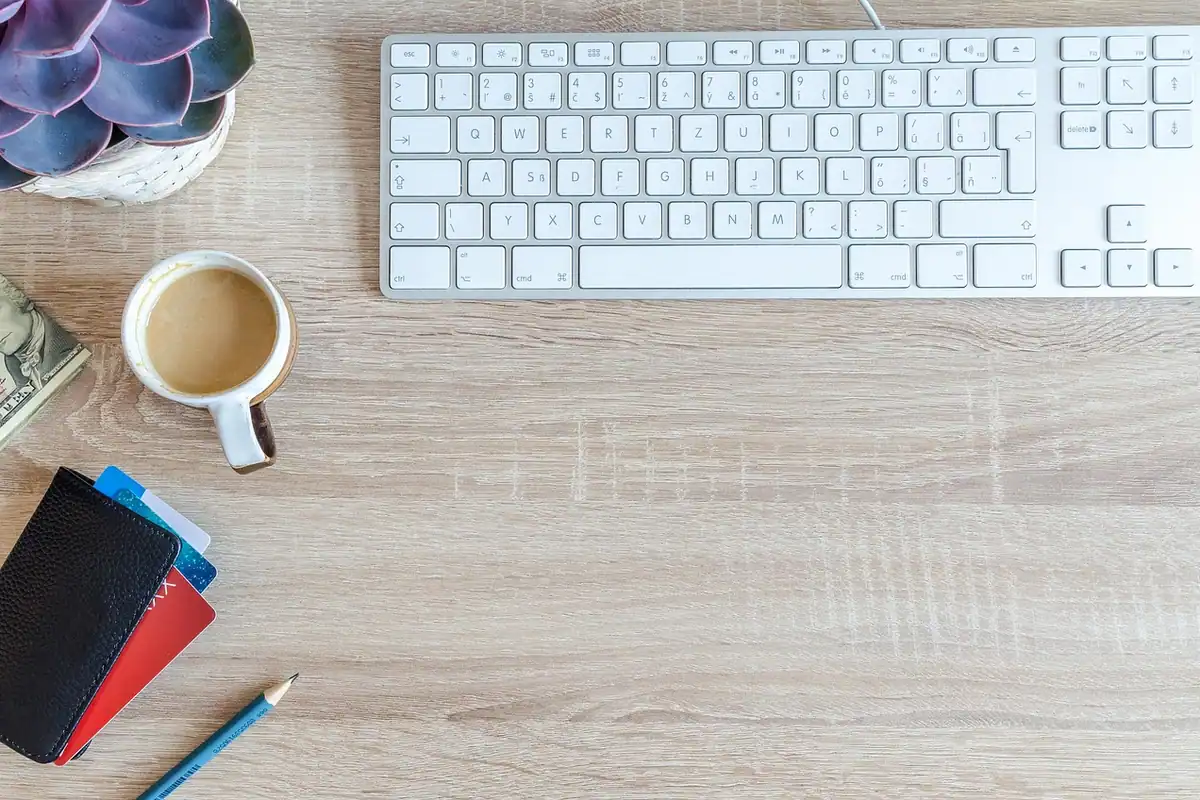 Birou cu tastatură, cană de cafea, carduri și un creion alături