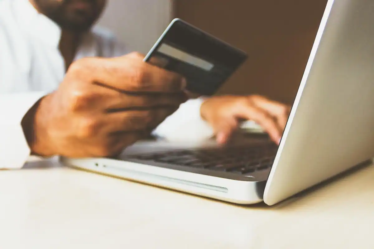 Persoană care ține un card bancar în fața laptopului, la plata online