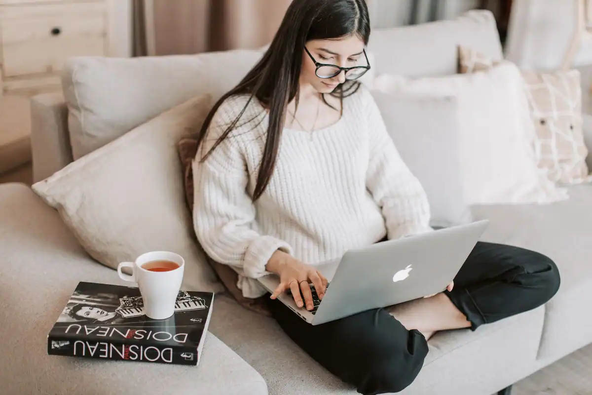 Femeie pe canapea care face o programare online de pe laptop