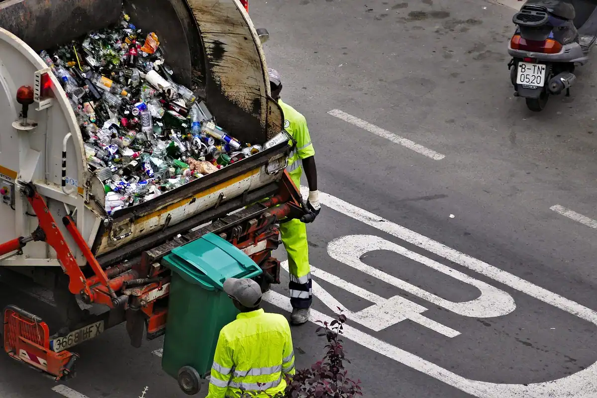 Lucrători în veste reflectorizante care golesc pubele într-un camion de gunoi