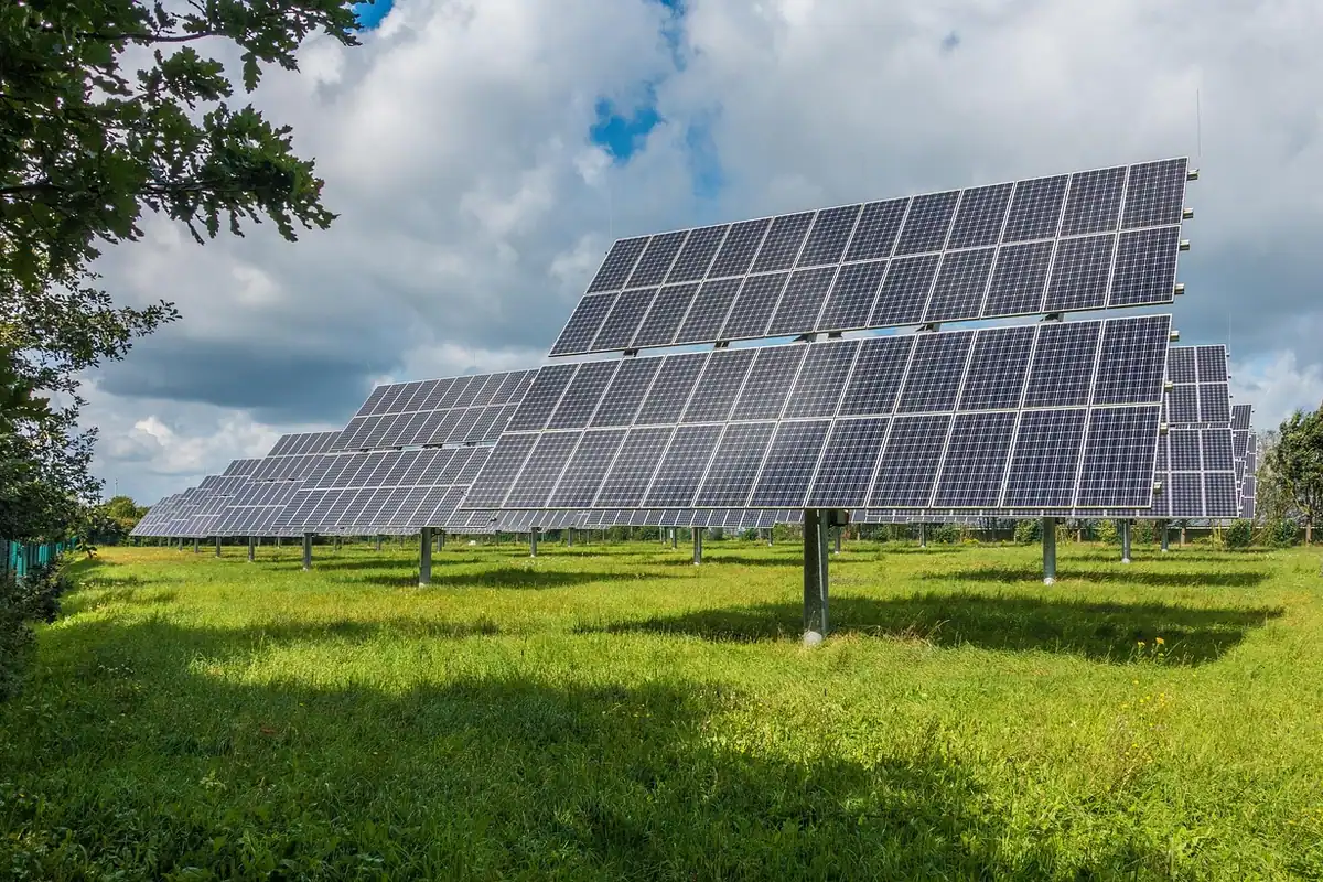 Panouri solare montate pe un câmp verde, sub un cer cu nori