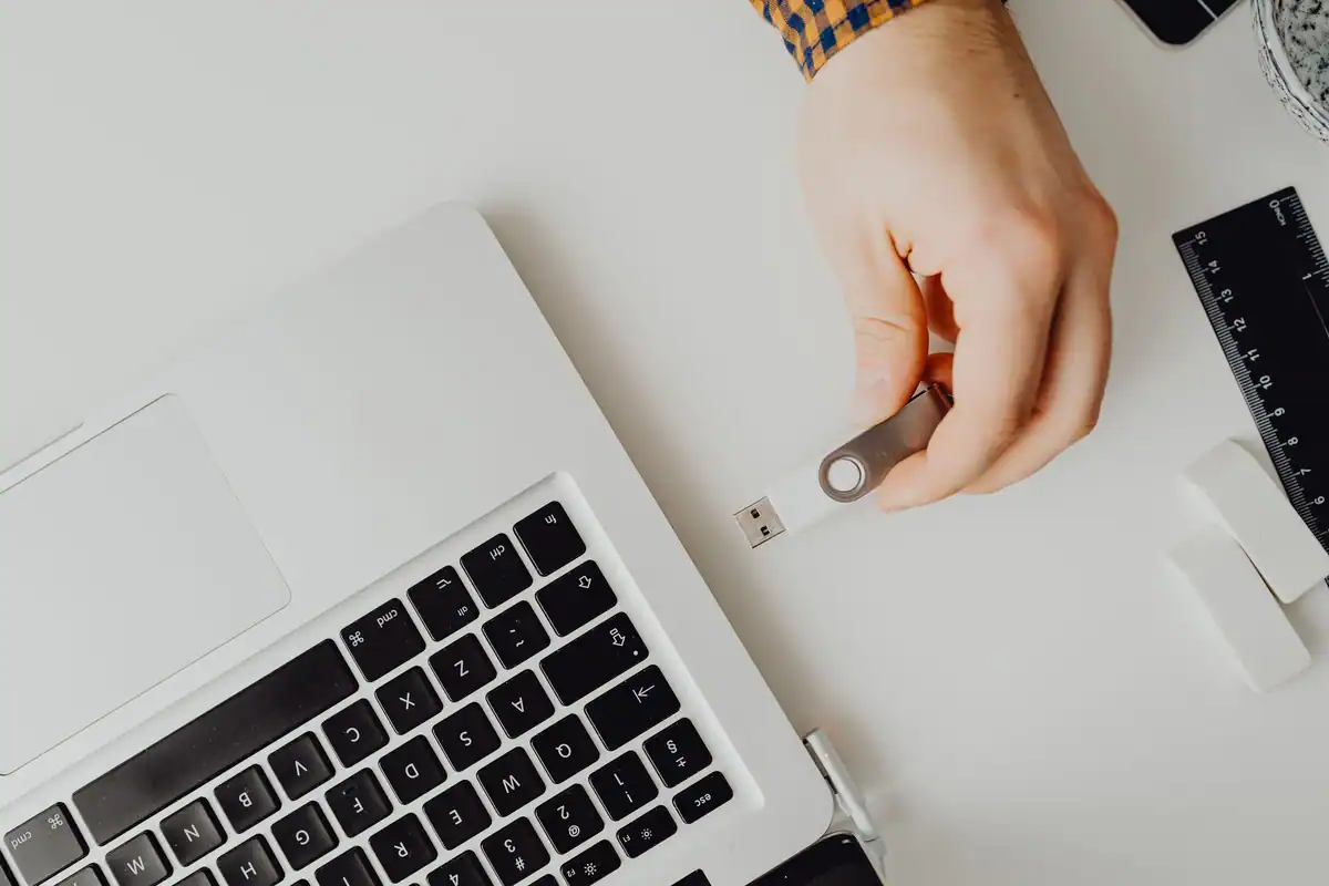 Stick USB conectat la un laptop alb, ținut între degete